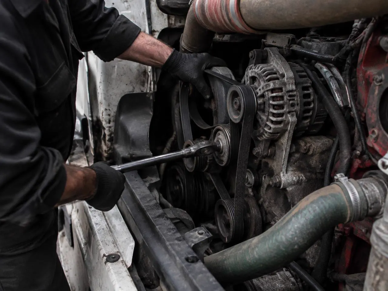 Gloved mechanic fitting a new serpentine belt and coolant hose on a semi truck diesel engine