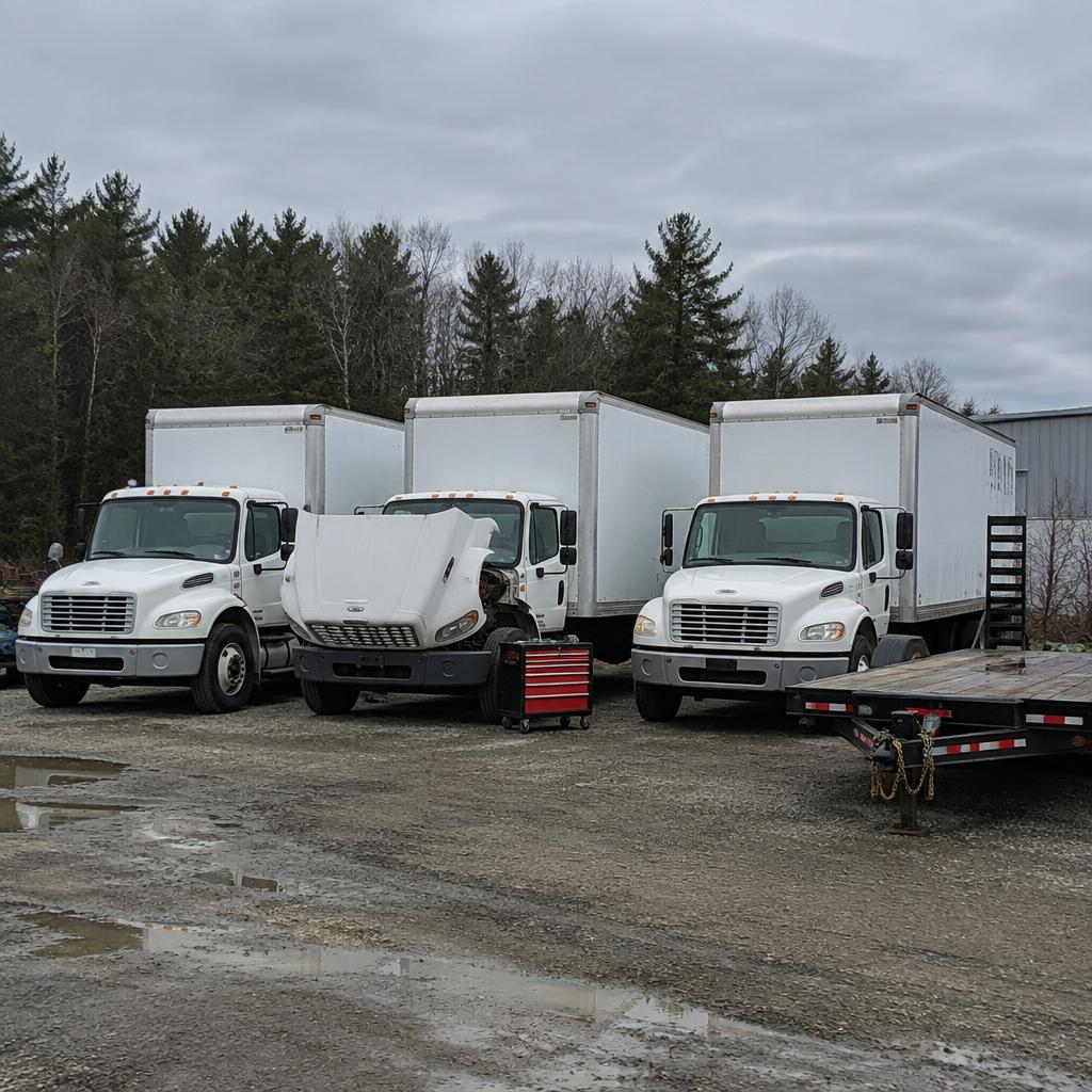 Fleet of white box trucks and an equipment trailer in a yard ready for fleet maintenance